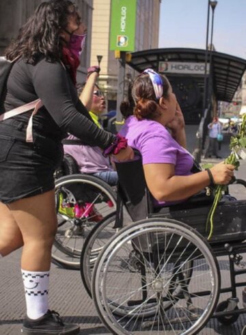 Una mujer empuja a otra mujer en silla de ruedas en la calle