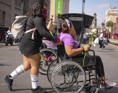 Una mujer empuja a otra mujer en silla de ruedas en la calle