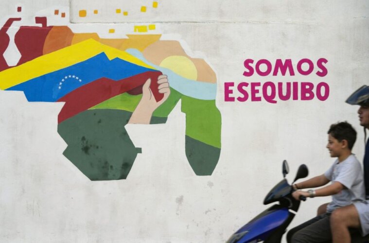 Un joven conduce una motocicleta frente a un mural con un mapa de Venezuela que incluye al territorio de Esequibo