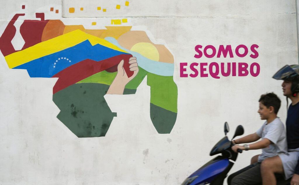 Un joven conduce una motocicleta frente a un mural con un mapa de Venezuela que incluye al territorio de Esequibo